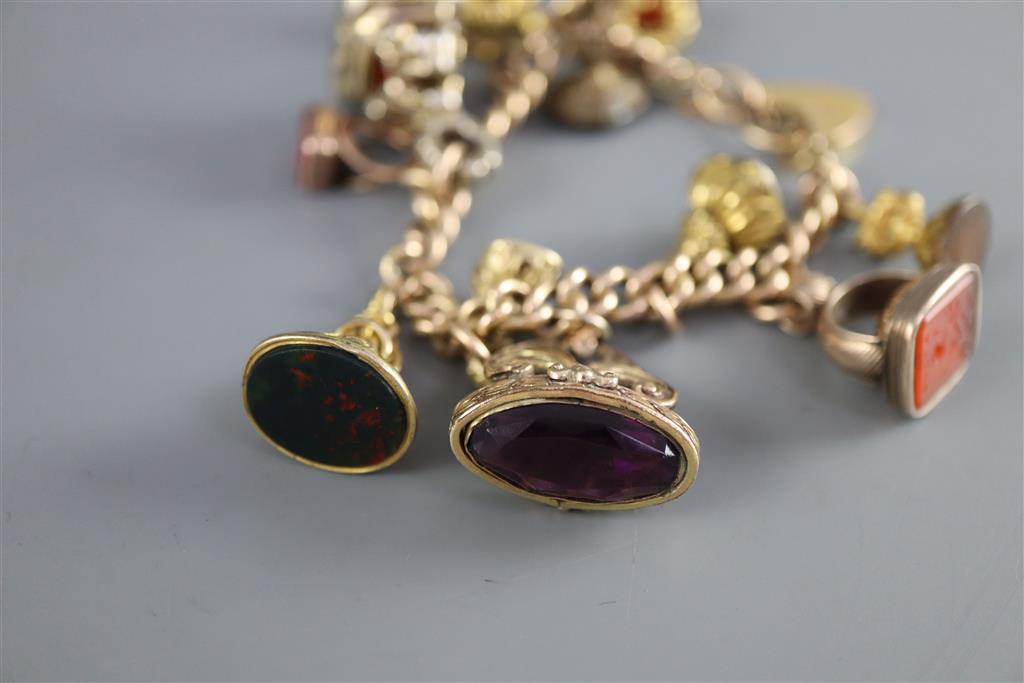 An early 20th century 9ct gold charm bracelet hung with thirteen assorted gold or gilt metal overlaid gem set fob seals,